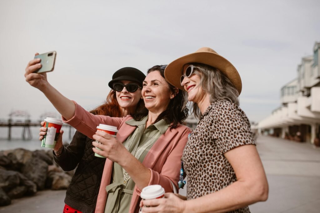 Three women enjoying coffee and taking a selfie together seaside.